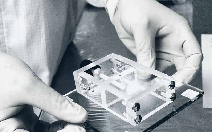 Técnico con guantes manipulando un componente dentro de un cuarto limpio